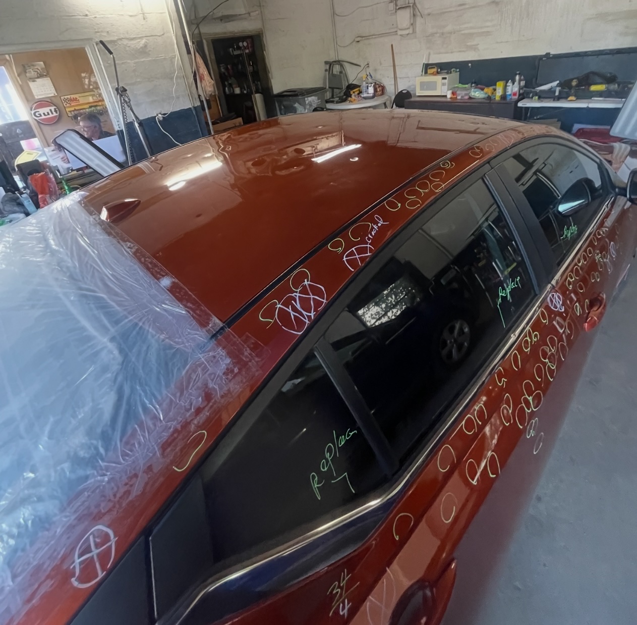 Hail damage marked up across the roof and body panels of a red car in our shop
