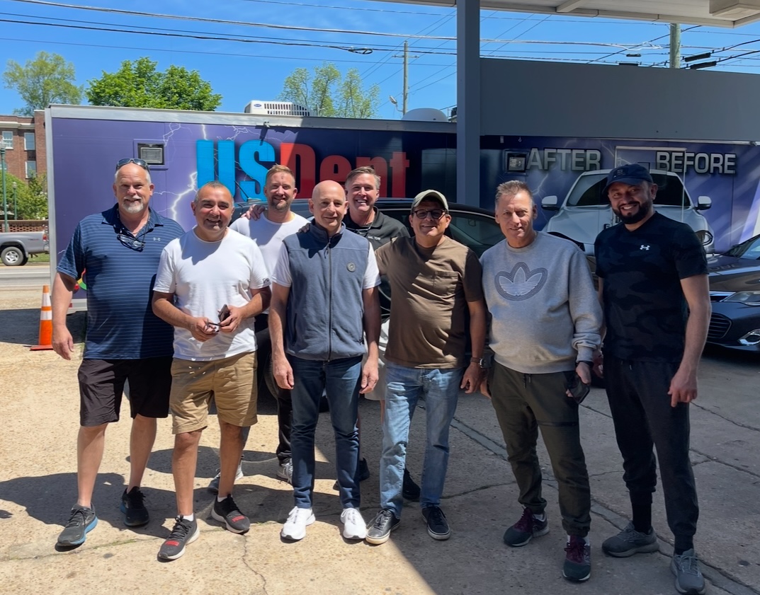 The US Dent Company team standing in front of their branded hail repair trailer